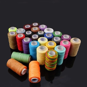 May include: A selection of colourful thread spools in shades like orange, green, yellow, blue, and pink. The spools are tightly arranged, displaying the range of colours and textures. Suitable for crafting and sewing projects.