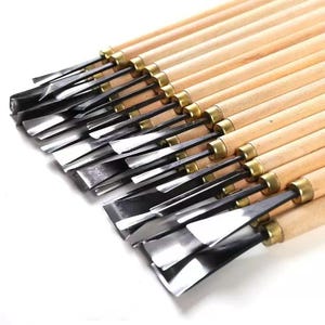 May include: A collection of wood carving tools with various blade shapes. The tools have wooden handles, brass ferrules, and polished steel blades. The blades are angled and flat, designed for detailed woodworking and carving projects.