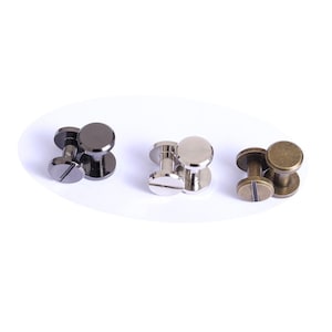 Op de afbeelding: Drie sets metalen klinknagels in verschillende afwerkingen: donkergrijs, zilver en antiek messing. Elke klinknagel bestaat uit een platte, sleufkop en een afgeronde dop, ontworpen om materialen te bevestigen. Ideaal voor leerbewerking en doe-het-zelf projecten.