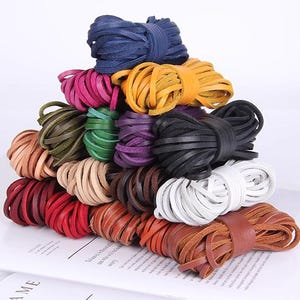 Puede incluir: Una colección de cordones de cuero coloridos en varios tonos, incluyendo azul, rosa, amarillo, verde, morado, negro, blanco y marrón. Los cordones están cuidadosamente agrupados y apilados, mostrando una gama de colores y texturas. Ideal para manualidades y joyería.