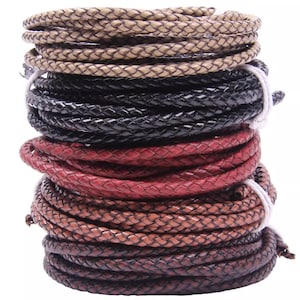 Puede incluir: Un montón de cordones de cuero trenzado en varios colores, incluyendo beige, negro, rojo y marrón. Los cordones están enrollados y asegurados con hilo blanco, mostrando una variedad de texturas y tonos. Ideal para la creación de joyas o proyectos de artesanía.