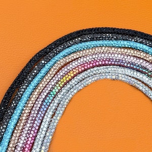 May include: A collection of curved, flexible cords covered in small, sparkling rhinestones arranged in a rainbow spectrum. The cords feature individual rows of black, turquoise, champagne, pink, yellow, green, and clear crystals in a dense pattern.