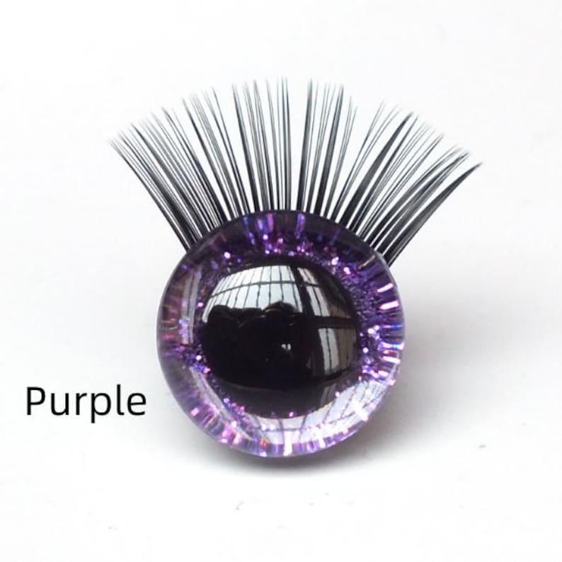 May include: A purple, glitter-encrusted glass eye with black eyelashes. The word "Purple" is printed in black text below the eye. The eye reflects the surrounding environment.