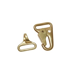 May include: Two brass-colored metal hardware pieces. One is a swivel hook with a spring-loaded clasp, and the other is a D-ring. Both pieces are new and appear to be unused. The hardware is likely for use in bags, belts, or other craft projects.
