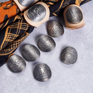 May include: A collection of coin-shaped rings and loose coins featuring state designs. The rings are made of light-colored wood and hold the coins. The coins display state names, dates, and imagery, including "CONNECTICUT" and "NEVADA".