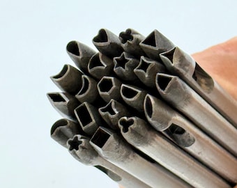 Könnte beinhalten: Eine Sammlung von Metall-Formstempeln, darunter Herzen, Sterne, Quadrate und Dreiecke. Die silberfarbenen Stempel haben verschiedene geometrische Formen am Schneidende. Die Werkzeuge sind für das Basteln und Erstellen von dekorativen Löchern konzipiert.