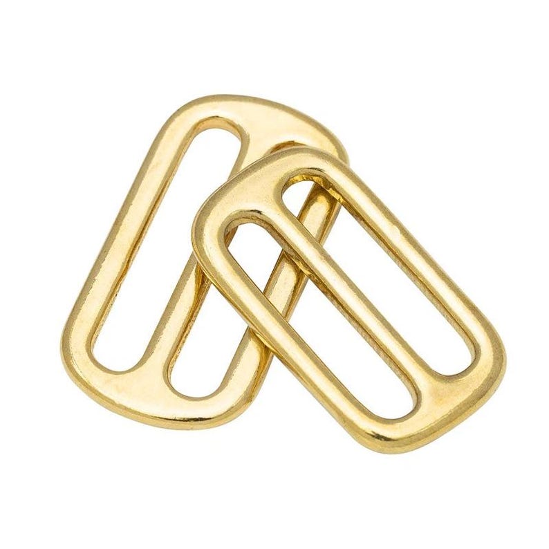 Op de afbeelding: Twee goudkleurige metalen rechthoekige ringen met afgeronde randen. De ringen overlappen elkaar licht, waarbij de ene voor de andere is geplaatst. De ringen hebben een glad, glanzend oppervlak en staan tegen een witte achtergrond.
