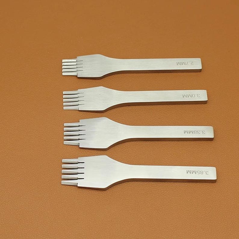 May include: Four silver leathercraft tools with multiple prongs. Each tool has a handle and is labeled with a measurement: 2.7MM, 3.0MM, 3.38MM, and 3.85MM. The tools are arranged on a brown surface.