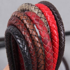 May include: A selection of braided leather cords in a range of colours: black, brown, red, and tan. The cords are closely woven, displaying a detailed texture. The image emphasizes the craftsmanship and the variety of colours available.