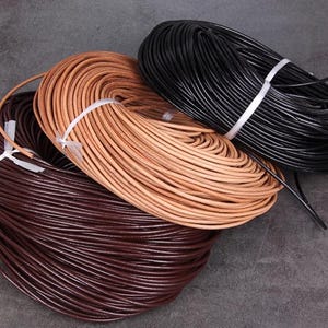Può includere: Tre rocchetti di cordoncino in pelle in varie tonalità di marrone e nero. I cordoncini sono avvolti strettamente e fissati con spago bianco. I colori vanno dal marrone scuro al marrone chiaro e nero, adatti per progetti artigianali.