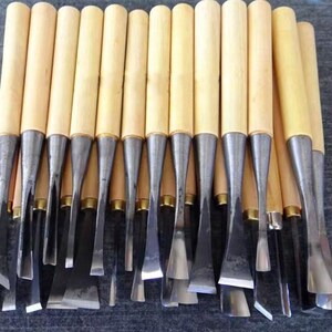 May include: A collection of wood carving chisels with light-colored wooden handles and silver-colored metal blades. The blades have various shapes and sizes, suitable for detailed woodworking projects.
