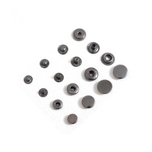 May include: An assortment of dark gray metal snap fasteners in various sizes, arranged on a white surface. The snaps include both male and female components, with different designs on the visible surfaces. The fasteners are likely for clothing or other fabric projects.