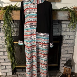 May include: A long-sleeved dress on a mannequin featuring a mock neck and a color-blocked design. The garment combines solid black fabric with a patterned section displaying horizontal stripes of leopard print, turquoise, and orange on a white base.