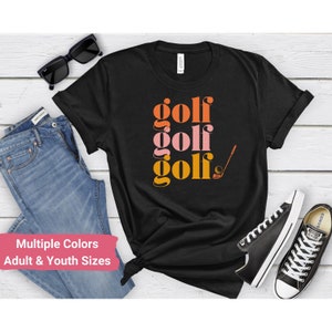 May include: Black t-shirt with the word "golf" repeated three times in stacked, stylized text. The word "golf" is in orange, pink, and yellow. A golf club and ball are to the right of the text.