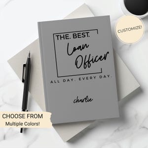 May include: Gray notebook with the text "THE. BEST. Loan Officer ALL DAY. EVERY DAY." and the name "charlie" written below. The notebook is on a white surface.