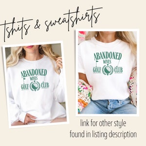 May include: Two white T-shirts with the text "Abandoned Wives Golf Club" in green lettering and a golf ball graphic. The shirts are shown on models wearing them.