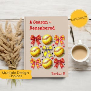 May include: A beige notebook with the text "A Season ~ Remembered" in red. The cover features softballs, red bows, and hearts. A yellow circle with "Customize!" is in the upper right. A pen and a cup of coffee are also visible.