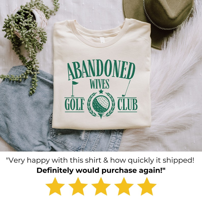 May include: A beige t-shirt with a green graphic that says "Abandoned Wives Golf Club". The graphic includes a golf club, a golf ball, and a flag.