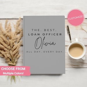 May include: Gray notebook with the text "THE. BEST. LOAN OFFICER Olivia ALL DAY. EVERY DAY."  The notebook is on a white wooden surface with a pen and a cup of coffee.