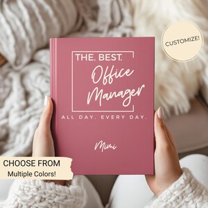 May include: A pink notebook with the text "THE. BEST. Office Manager ALL DAY. EVERY DAY." and a customizable name field. The text is in white. The notebook is on a white fuzzy surface.