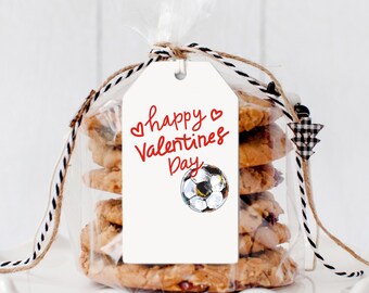 Puede incluir: Una bolsa transparente de celofán atada con hilo, que contiene varias galletas. Una etiqueta blanca con las palabras "happy Valentines Day" y una ilustración de balón de fútbol está adjunta a la bolsa.