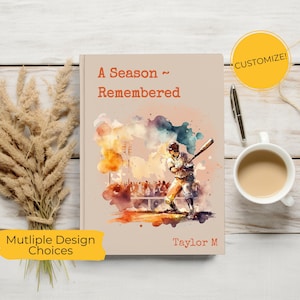 May include: A beige notebook with the title "A Season Remembered" and a watercolor illustration of a baseball player. The notebook has a customizable option and multiple design choices. A pen and a cup of coffee are next to the notebook.