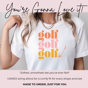 May include: White t-shirt with the word "golf" repeated three times in stacked, overlapping, colorful text. The top word is orange, the middle word is pink, and the bottom word is yellow. A golf club and ball are to the right of the text.