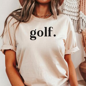 Woman wearing a beige “golf.” t-shirt tucked into jeans — simple and stylish golf shirt for everyday wear.