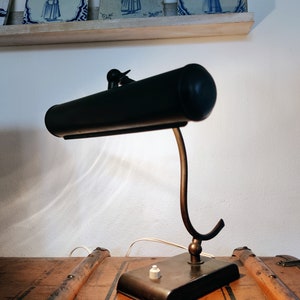 May include: A black vintage desk lamp with a long, curved arm and a black shade. The lamp has a brass base and a white switch.