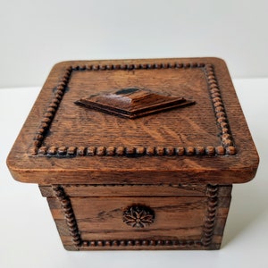May include: A wooden box with a carved design on the lid and sides. The box is dark brown and has a small, square knob on the top.