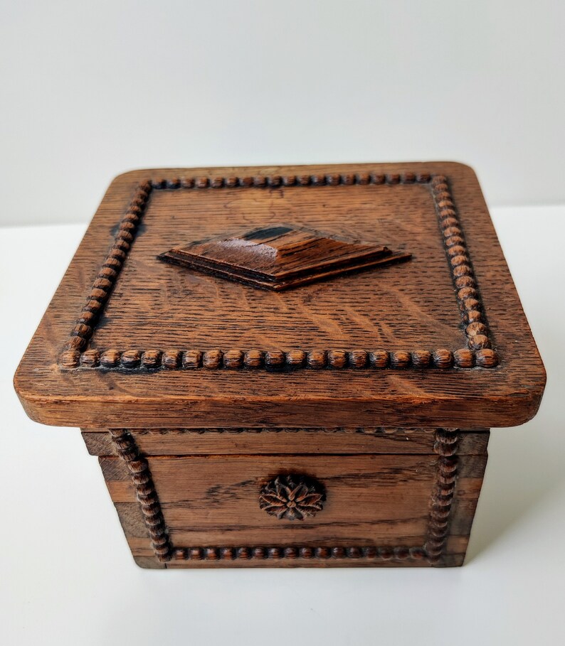 May include: A wooden box with a carved design on the lid and sides. The box is dark brown and has a small, square knob on the top.