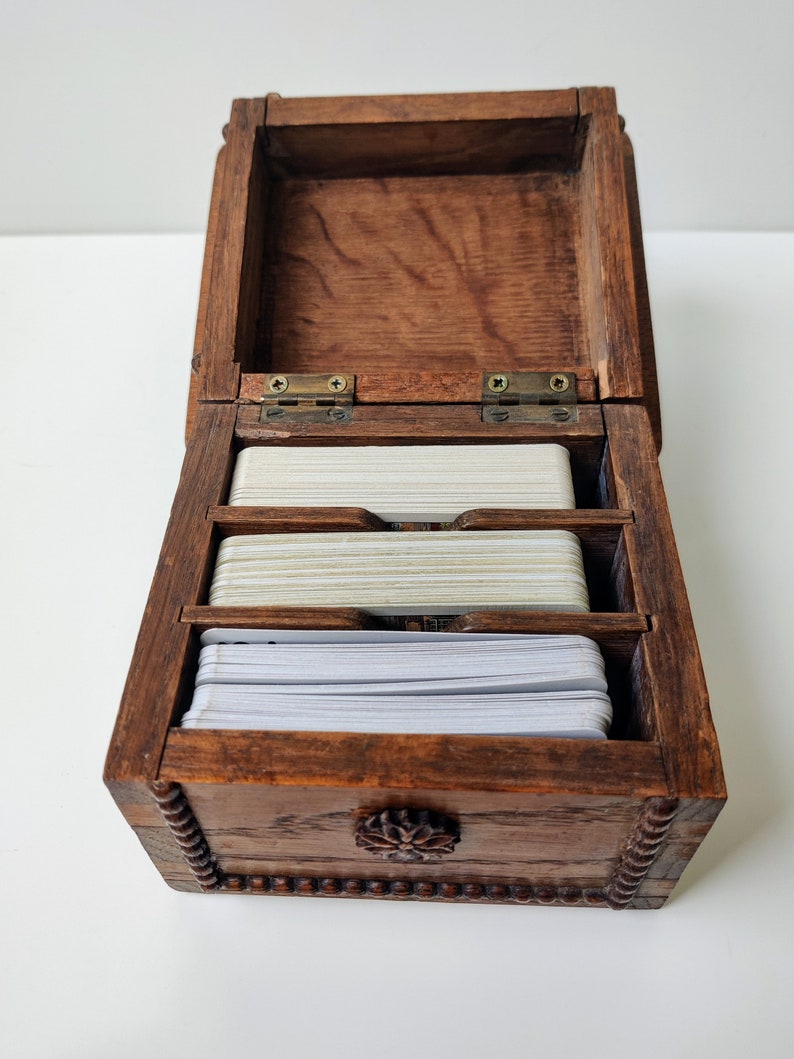 May include: A wooden box with a hinged lid and a carved floral design on the front. The box is open and contains three stacks of white cards.