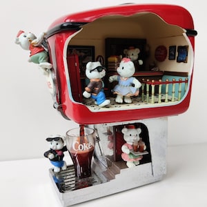 May include: A red Coca-Cola themed miniature diner with a white roof and a silver base. The diner has a window with a Coca-Cola sign and a small interior with five white polar bear figurines. One polar bear is climbing a ladder, one is serving drinks, and three are inside the diner. The diner is pouring a glass of Coca-Cola.