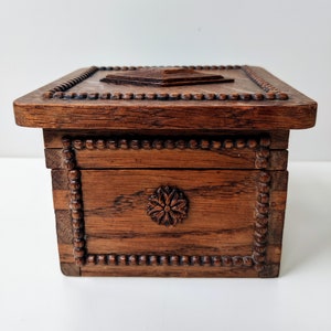May include: A wooden box with a carved floral design on the front and a beaded border around the edges. The box has a hinged lid with a carved design on top.