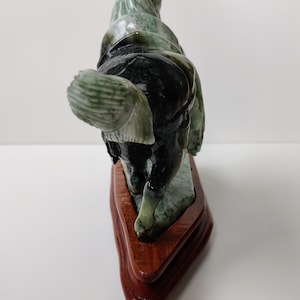 May include: A green jade horse sculpture on a wooden stand. The horse is carved in a standing pose with its head turned to the side. The jade is a mottled green colour with black and white streaks.