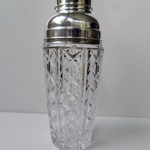May include: A silver-plated cocktail shaker with a clear glass body featuring a cut-glass design.