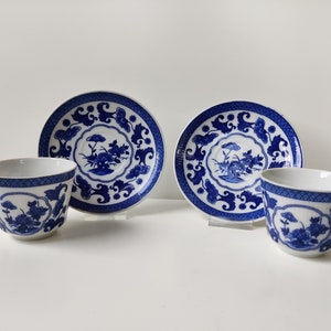 May include: Two blue and white porcelain teacups and saucers with a floral design. The cups and saucers have a white background with blue floral patterns.
