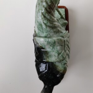May include: A green and black jade sculpture of a person riding a horse. The sculpture is mounted on a wooden base.