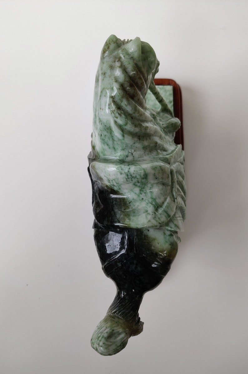 May include: A green and black jade sculpture of a person riding a horse. The sculpture is mounted on a wooden base.