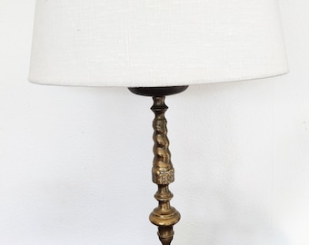 May include: An antique brass table lamp with a white linen lampshade. The lamp features a detailed, ornate base and a twisted column. The shade is a classic, tapered shape, providing soft, ambient lighting. A decorative piece for any room.