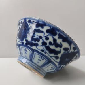 Puede incluir: Un pequeño cuenco de porcelana azul y blanco con un diseño floral. El cuenco está decorado con un patrón repetitivo de flores y hojas.