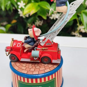 Puede incluir: Una figura caprichosa de un camión de bomberos rojo con una escalera, con dos ratones con atuendo de bombero. El camión tiene las letras "F.D." en la parte delantera. La base de la figura tiene las palabras "FIRE DEPARTMENT".