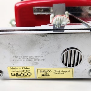 May include: A red and chrome musical clock with a Coca-Cola theme. The clock is made in China exclusively for Enesco Corporation. The clock features a label that reads "Rock Around The Clock" and "Musical".