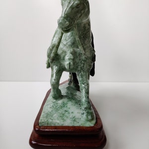 May include: A green jade horse sculpture on a wooden base. The horse is standing on its hind legs with its front legs raised. The sculpture is detailed and intricate.