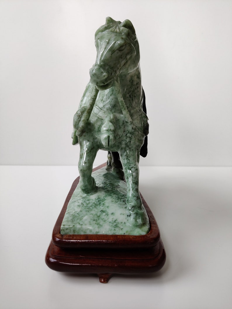 May include: A green jade horse sculpture on a wooden base. The horse is standing on its hind legs with its front legs raised. The sculpture is detailed and intricate.