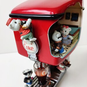 May include: A red Coca-Cola dispenser with a white 'Have a Coke' sign.  The dispenser has a glass of cola being poured and three small white bear figurines.  One bear is climbing the side of the dispenser, one is holding a glass of cola, and one is inside the dispenser.