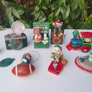 Op de afbeelding: Een verzameling kerstversieringen met verschillende ontwerpen. Inclusief een camera met een krans, een trein, een voetbal en dierenbeeldjes. De ornamenten zijn kleurrijk en gedetailleerd, perfect voor de feestdagen.