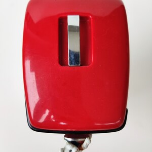 May include: A red plastic mouse trap with a silver metal trigger. The trap is designed to catch mice.