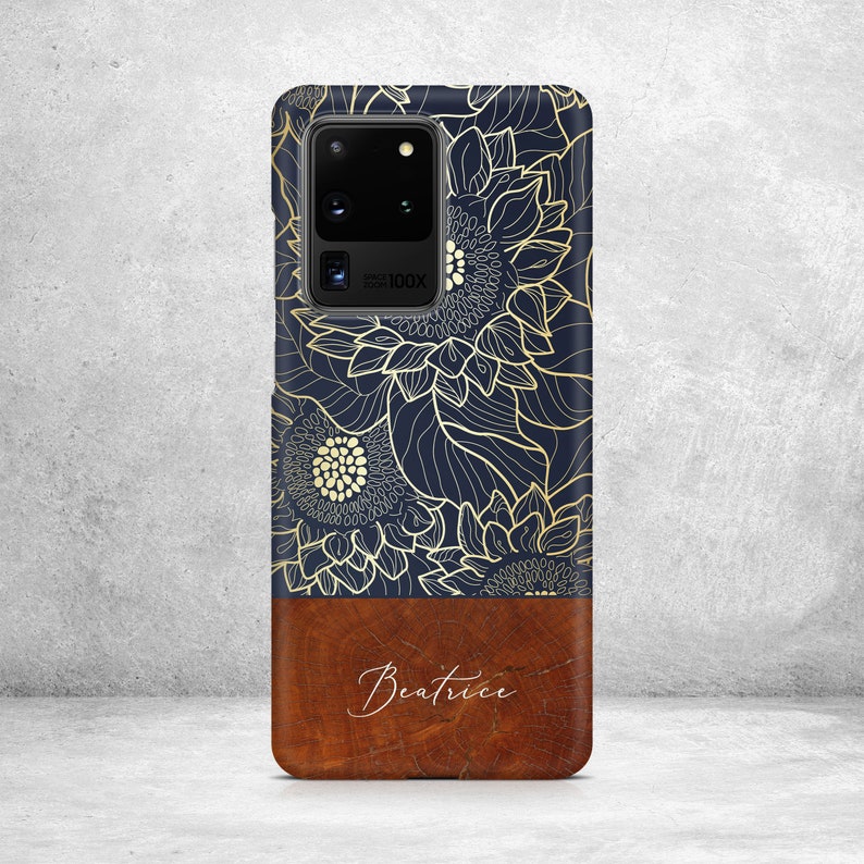 May include: A navy blue phone case with a gold floral design and a brown wood-grain bottom with the name "Beatrice" written in white.