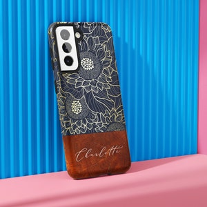 May include: A navy blue phone case with a gold sunflower design and a brown leather bottom with the name "Charlotte" written in white.